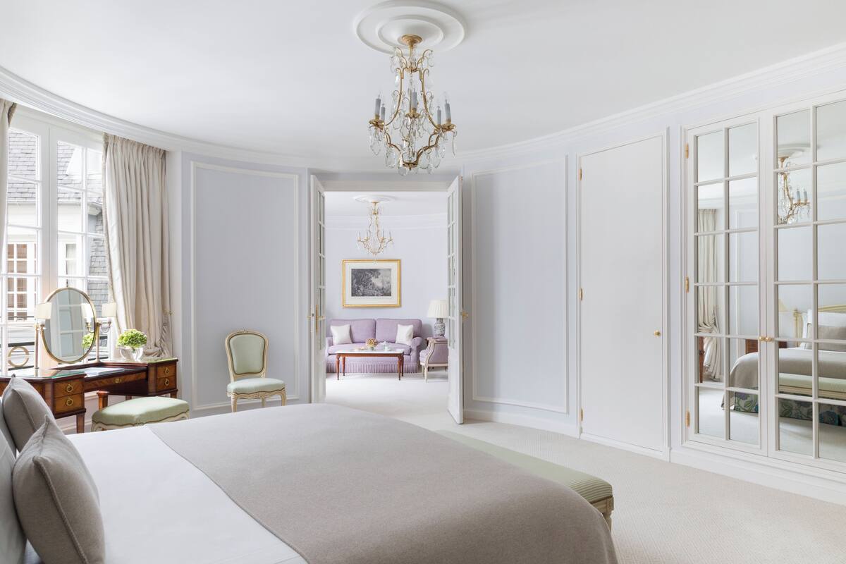A spacious bedroom with a large bed, a vanity with a mirror, and a chandelier.