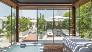 A modern outdoor hot tub area with a wooden deck, a lounge chair, and a view of a garden and patio area. - Le Bristol Paris - Oetker Hotels (Paris)