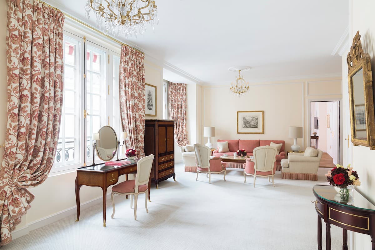 A room with a desk, chairs, a sofa, and a chandelier.