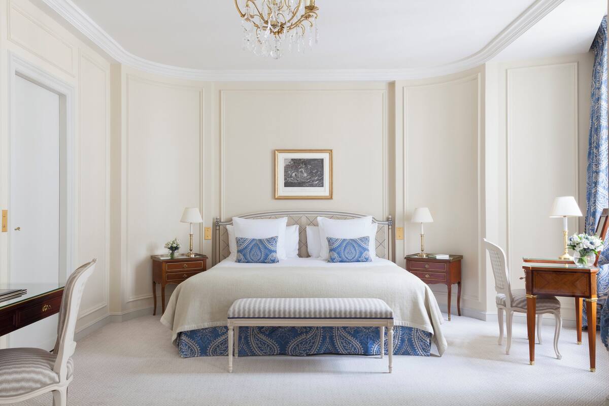 A spacious bedroom with a large bed, bedside tables, a bench, and a chandelier.