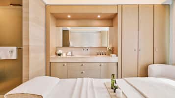 A modern hotel room with a large bed, a bathroom with a shower, and a vanity with a mirror.