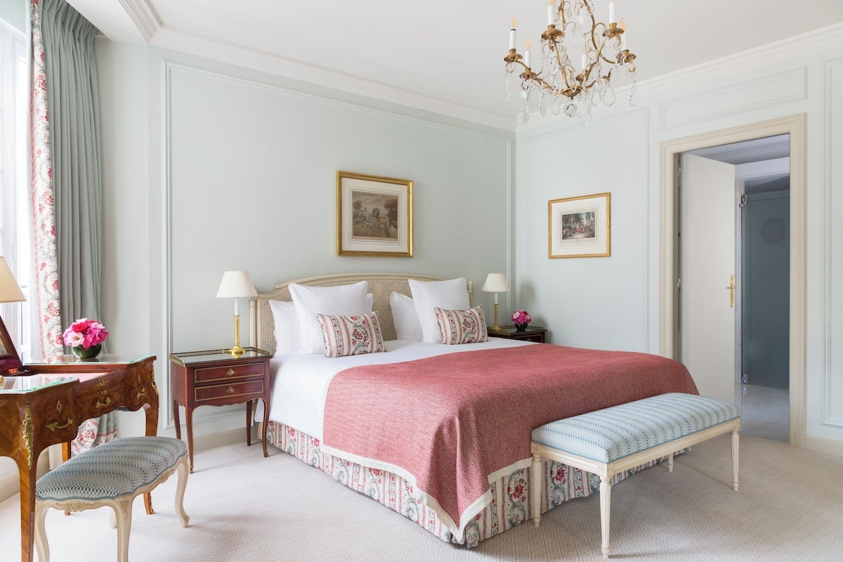 A neatly arranged bedroom with a large bed, bedside tables, a bench, and a chandelier.