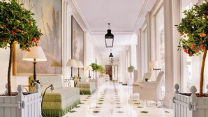 A hotel corridor with a polished floor, white furniture, and potted plants with fruit-bearing trees.