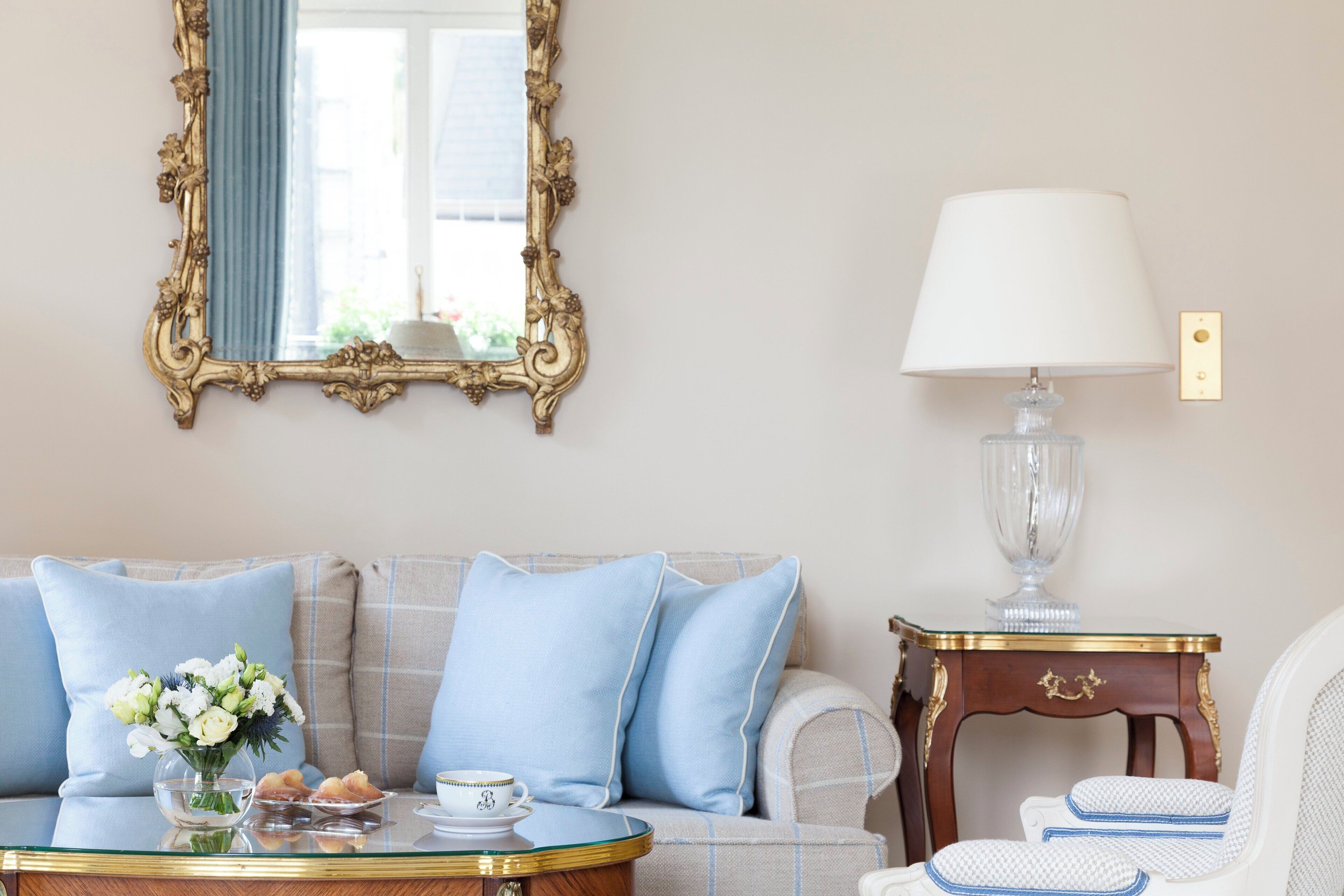 Una habitación con un sofá, una mesa con un florero, una lámpara y un espejo con un marco decorativo.