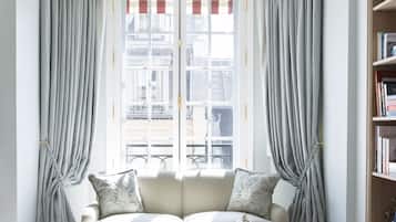 A room with a sofa, a table, and a chair. There is a window with curtains and a chandelier.