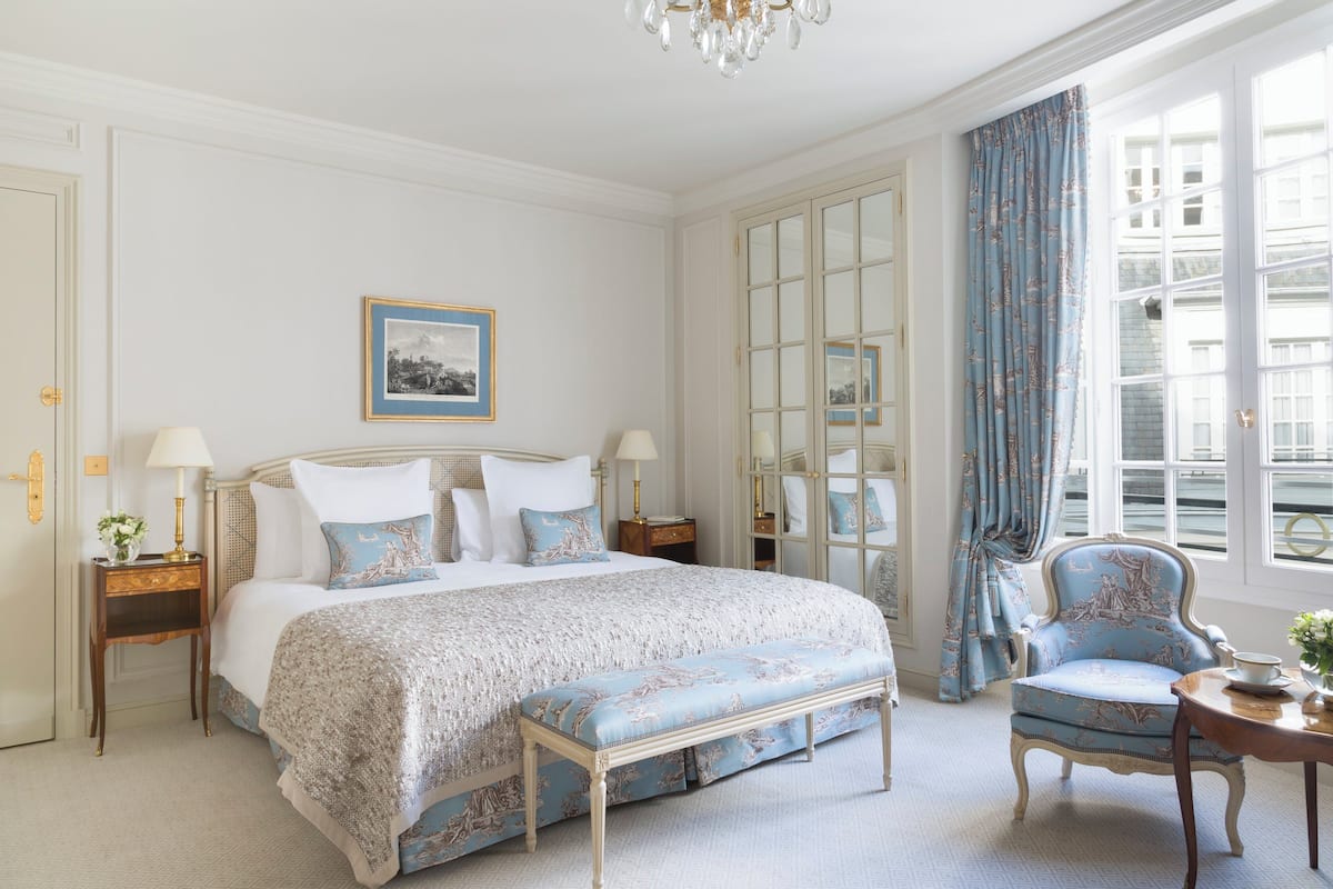 A classic bedroom with a large bed, a bench, a chair, and a mirror.