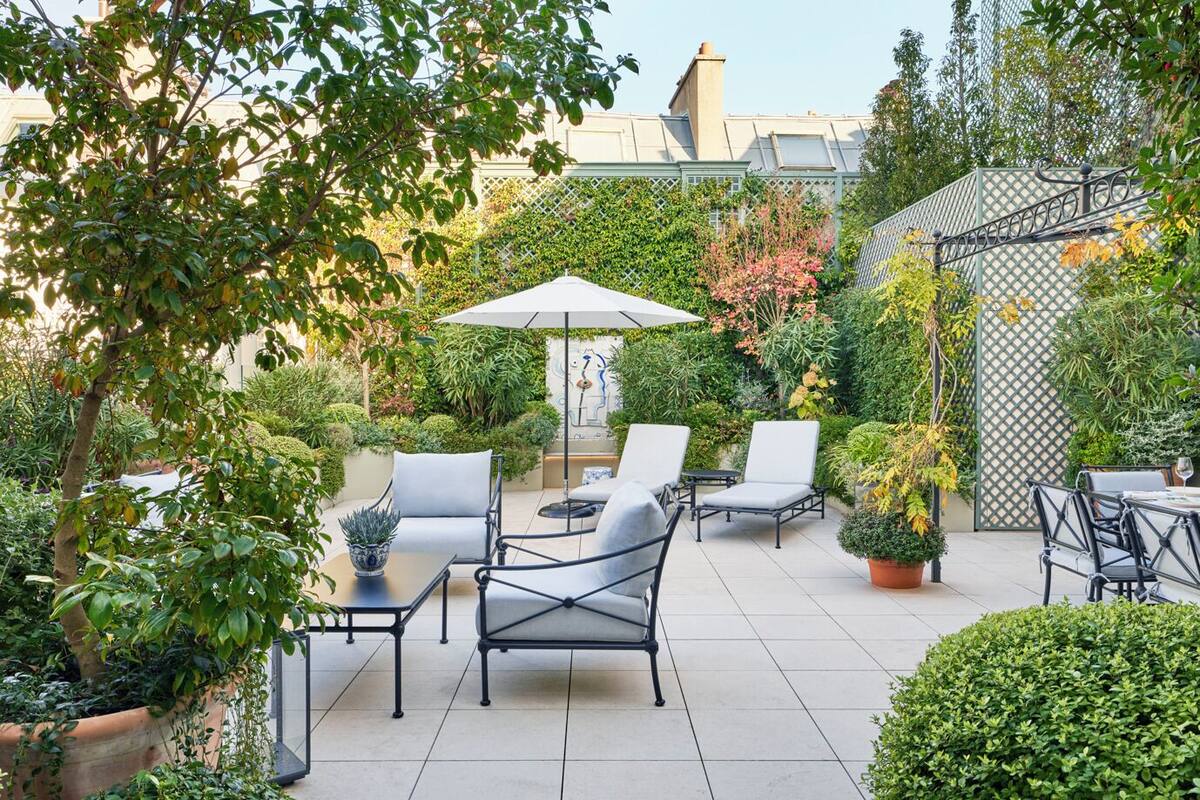 An outdoor patio with a table and chairs, surrounded by lush greenery and a decorative fence.