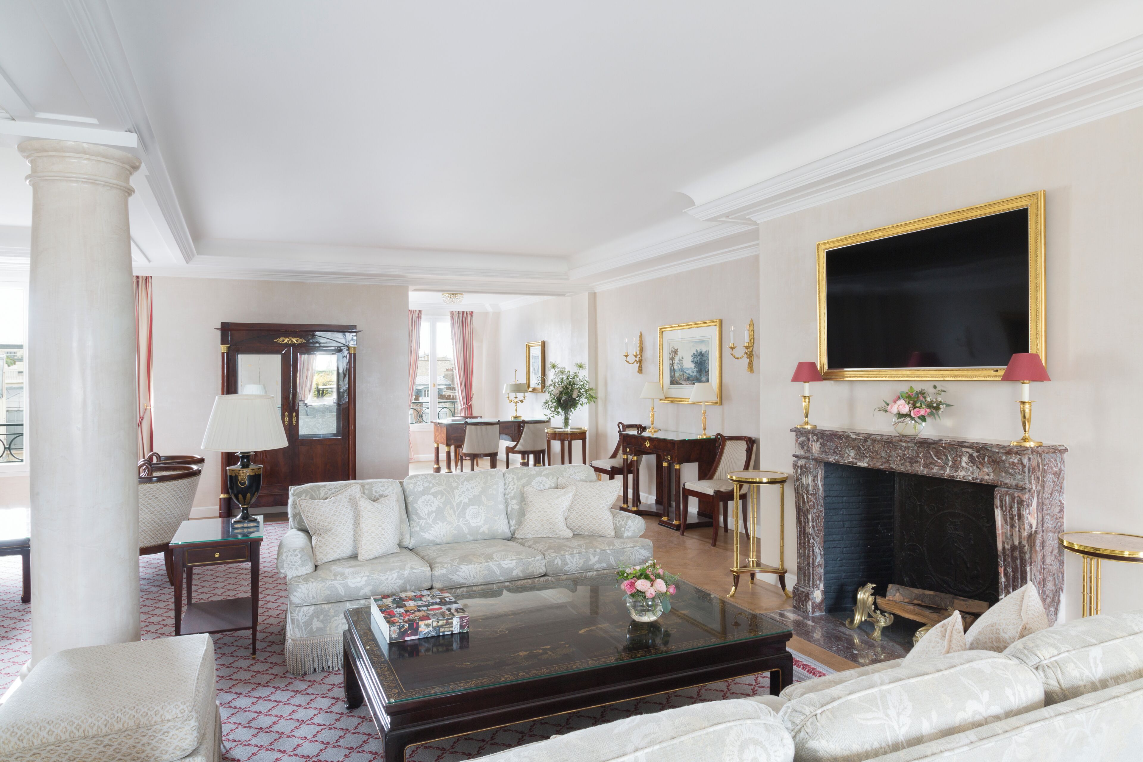 A spacious living room with a fireplace, a sofa set, a coffee table, and a dining area in the background.