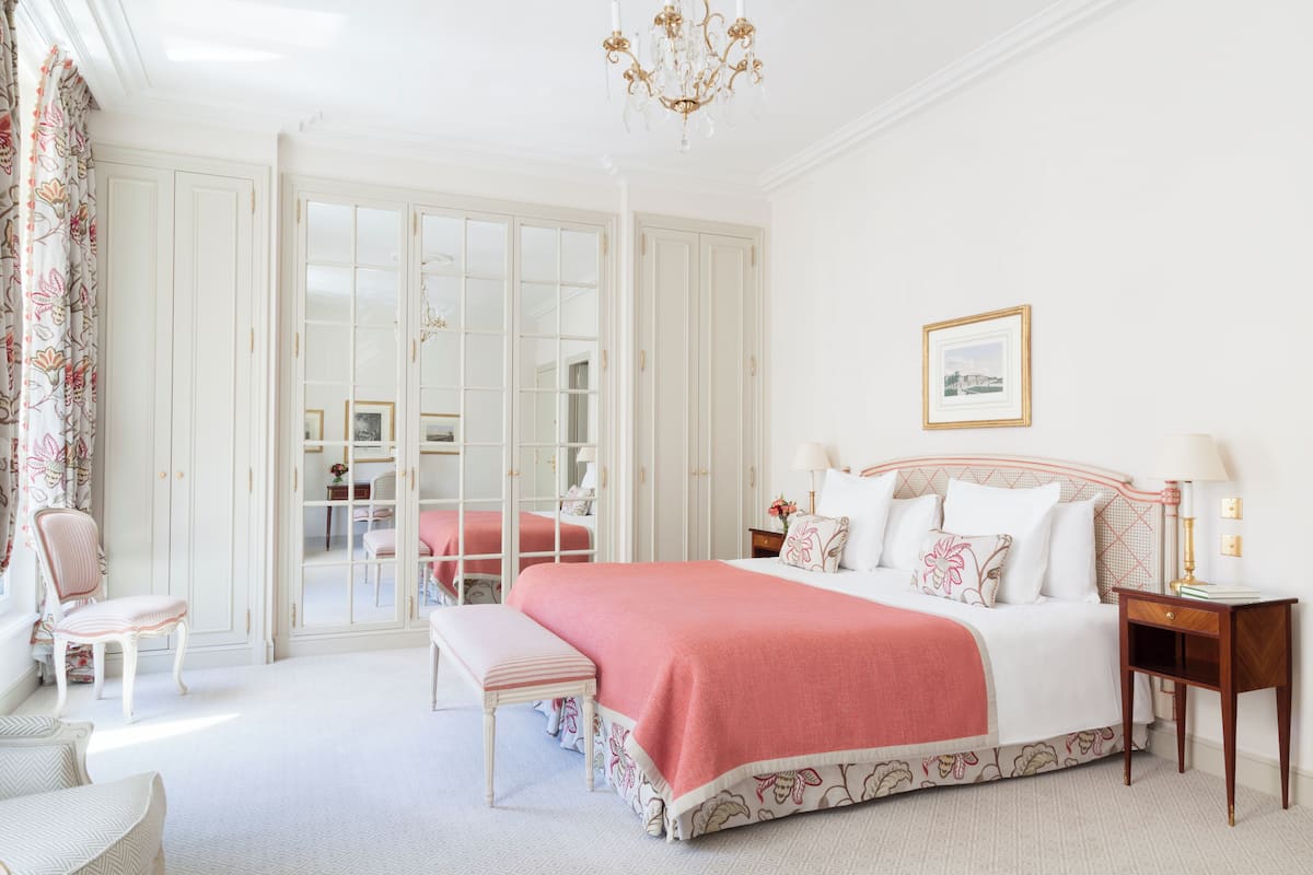A bedroom with a large bed, a bench, a chair, a nightstand, and a chandelier.