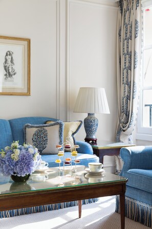 A living room with a blue sofa, a glass coffee table with a vase of flowers, a lamp, and a framed picture on the wall.