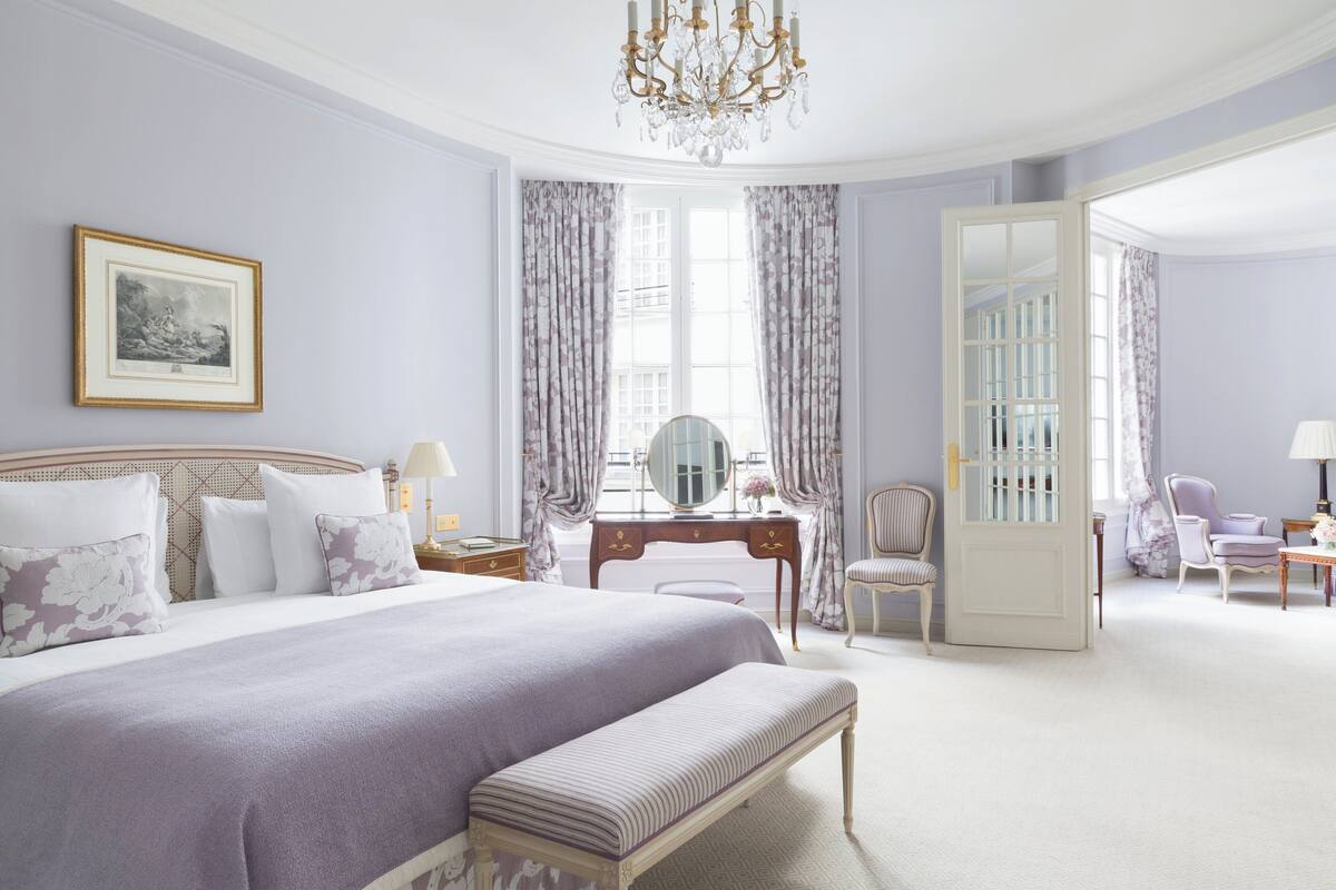 A bedroom with a large bed, a vanity with a mirror, a chair, and a desk with a lamp.