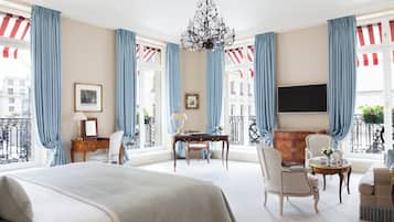 A spacious hotel room with a large bed, a desk, two chairs, a sofa, and a TV.