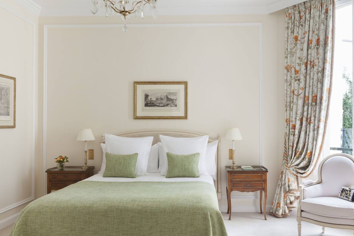A neatly arranged bedroom with a large bed, two bedside tables with lamps, a chair, and a framed picture on the wall.