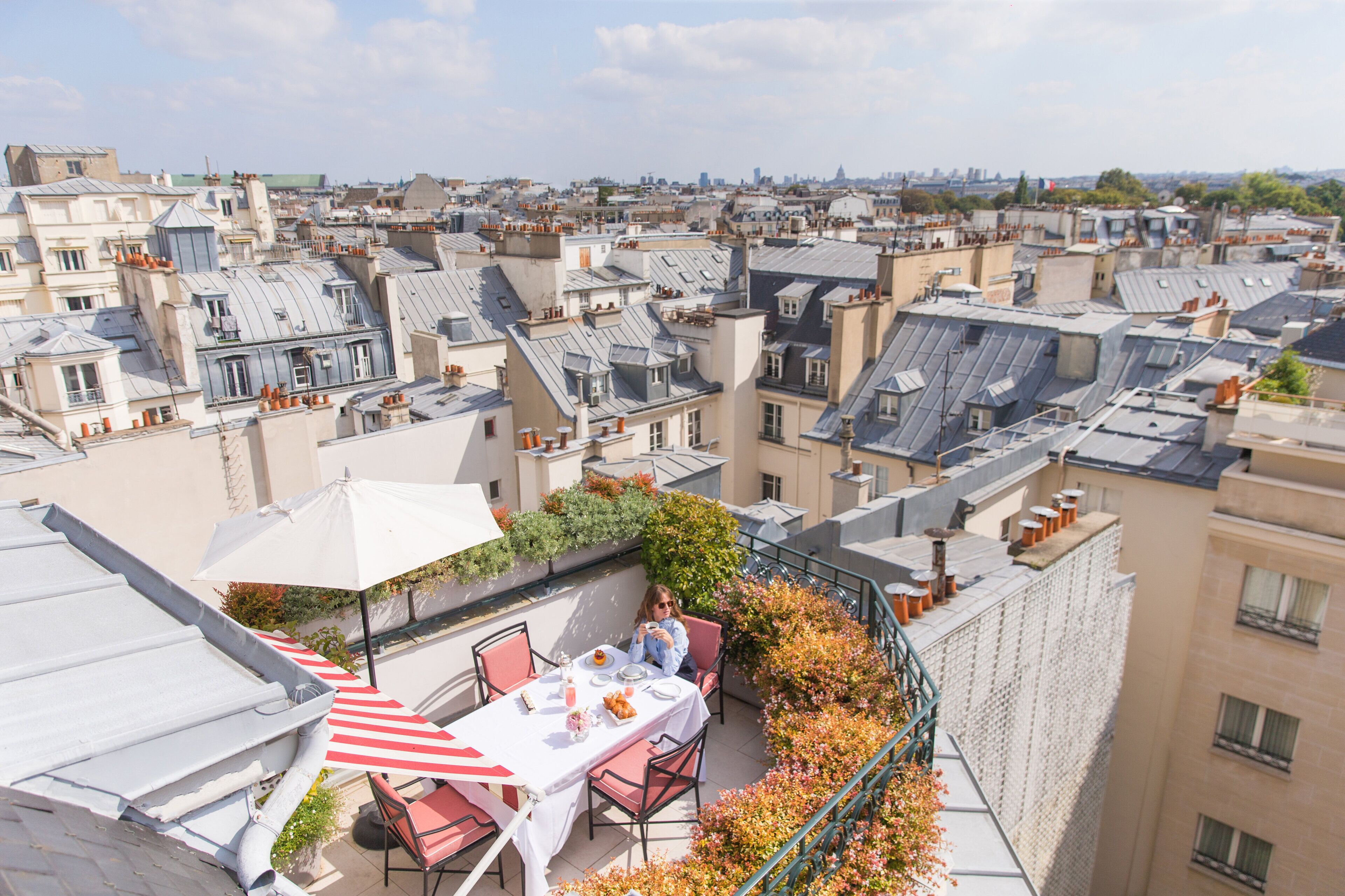 A rooftop terrace with a dining table, chairs, and a striped umbrella.