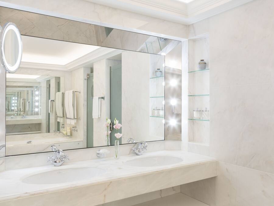 A modern bathroom with two sinks, a large mirror, and a glass shelf with toiletries.