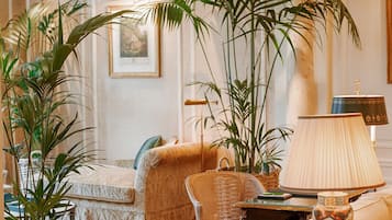 A well-lit living room with a sofa, a wicker side table, a lamp, and several potted plants.