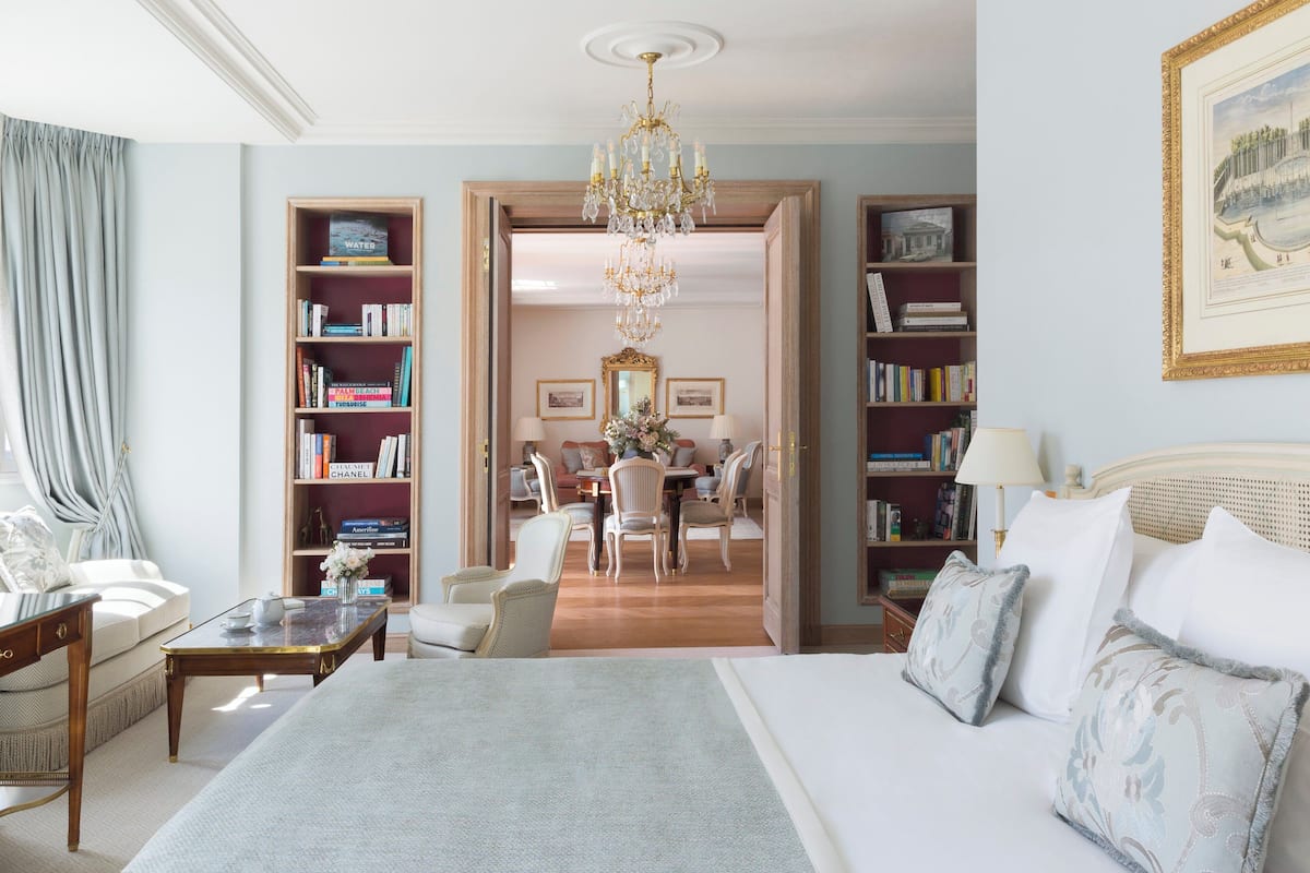 A spacious hotel room with a large bed, a sitting area with a coffee table, and two bookshelves filled with books.