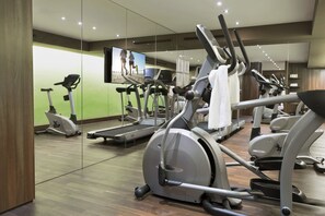 A gym with stationary bikes, treadmills, and a TV screen displaying an image of people running.