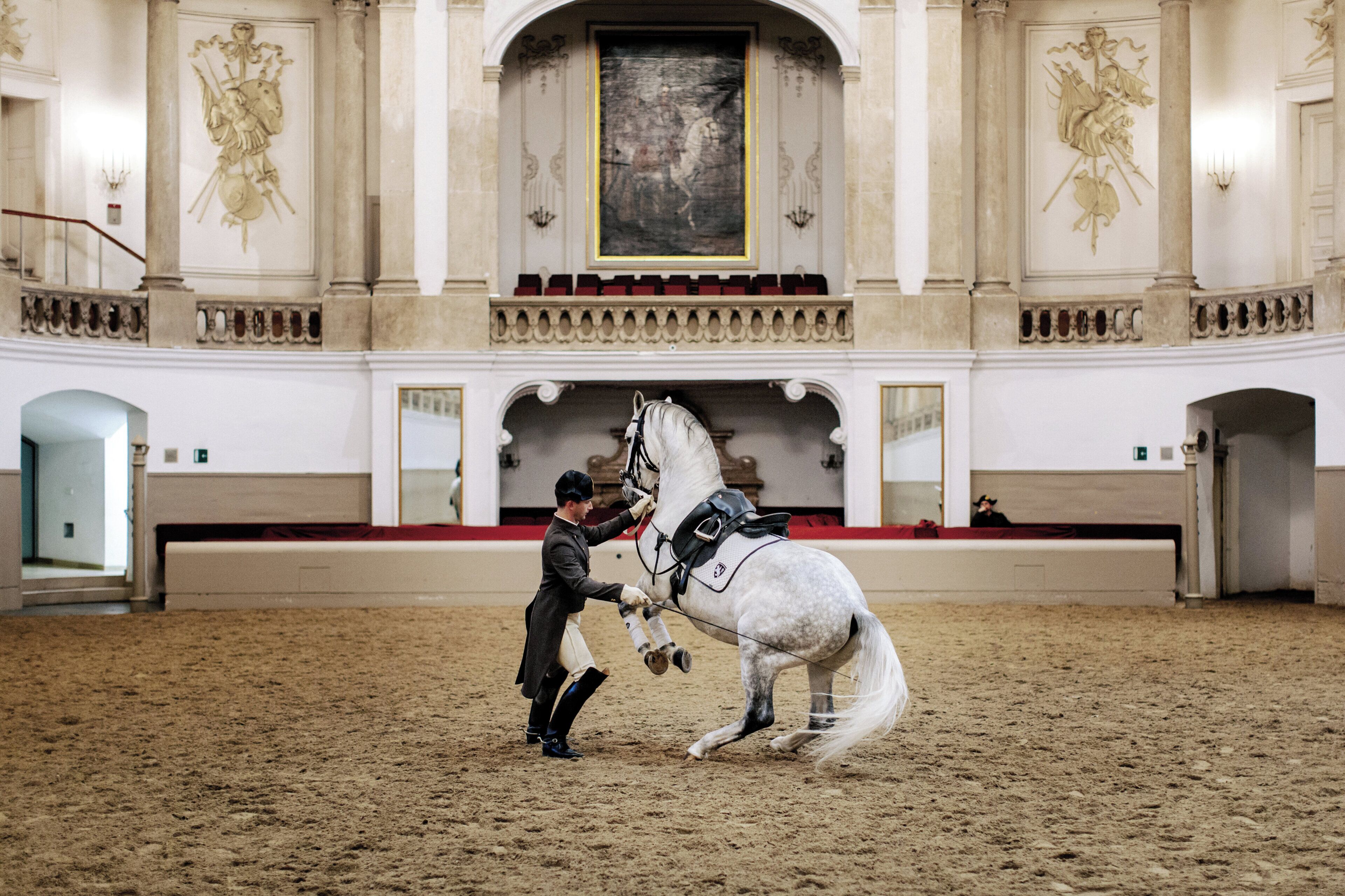 A horse and rider in an indoor arena with classical architecture, including columns and a high ceiling.
