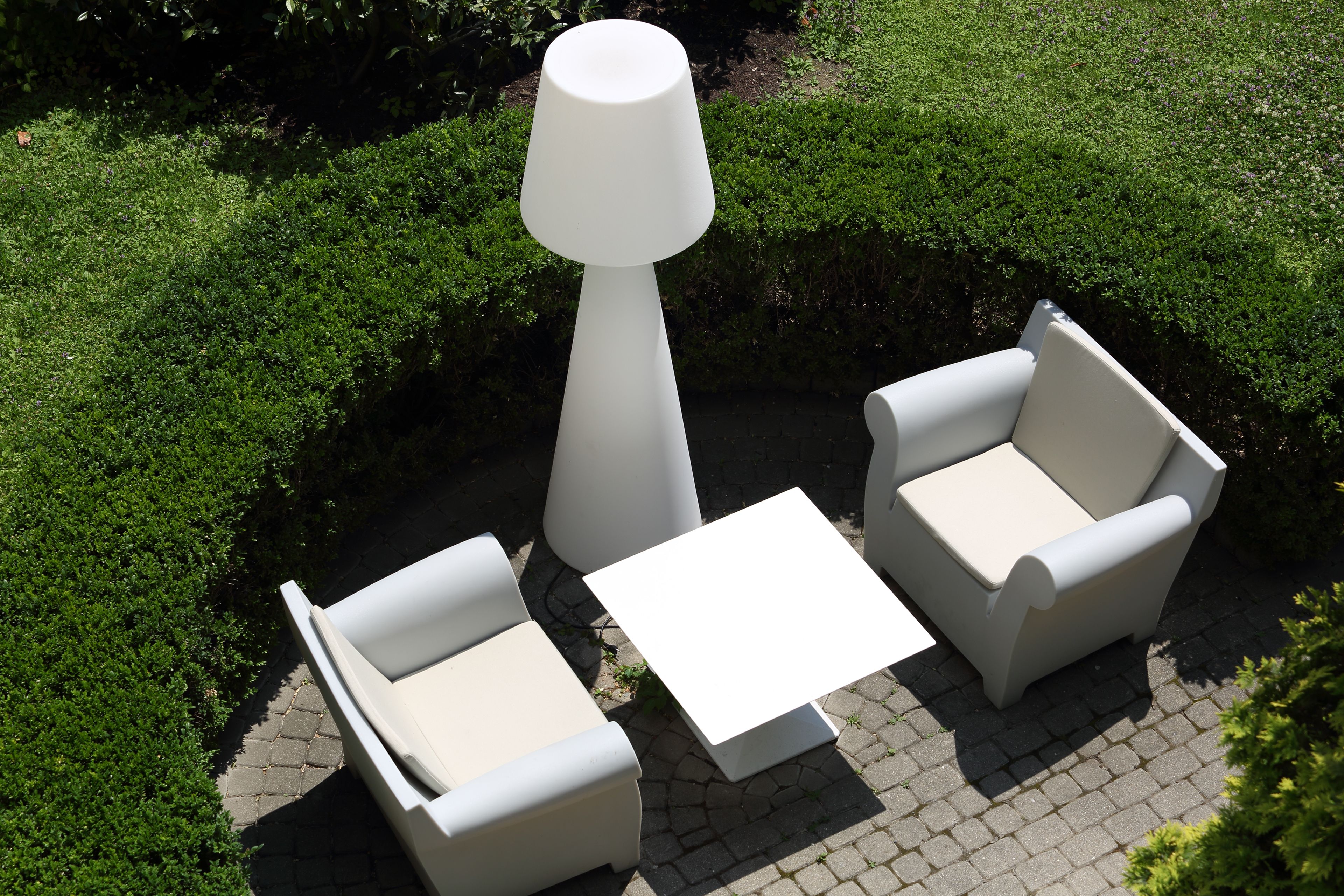 A patio area with two white armchairs, a small white table, and a tall white lamp.