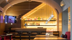 A bar area with a wooden ceiling, hanging lights, and a bar stocked with various bottles. There are stools and a table with a teapot. - Holiday Inn Vienna City by IHG (Vienna)