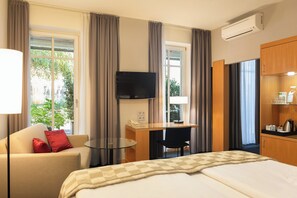 A hotel room with a bed, a desk, a chair, a TV, and a window with curtains.