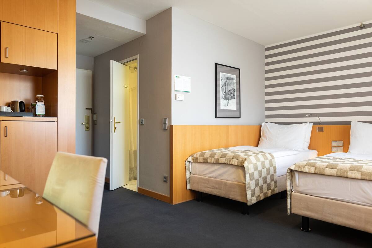 Une chambre d’hôtel avec deux lits, une tête de lit en bois, un tableau encadré au mur et une petite table avec une chaise.
