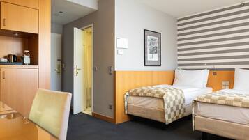 Quarto de hotel com duas camas, uma cabeceira de madeira, um quadro na parede e uma pequena mesa com uma cadeira.