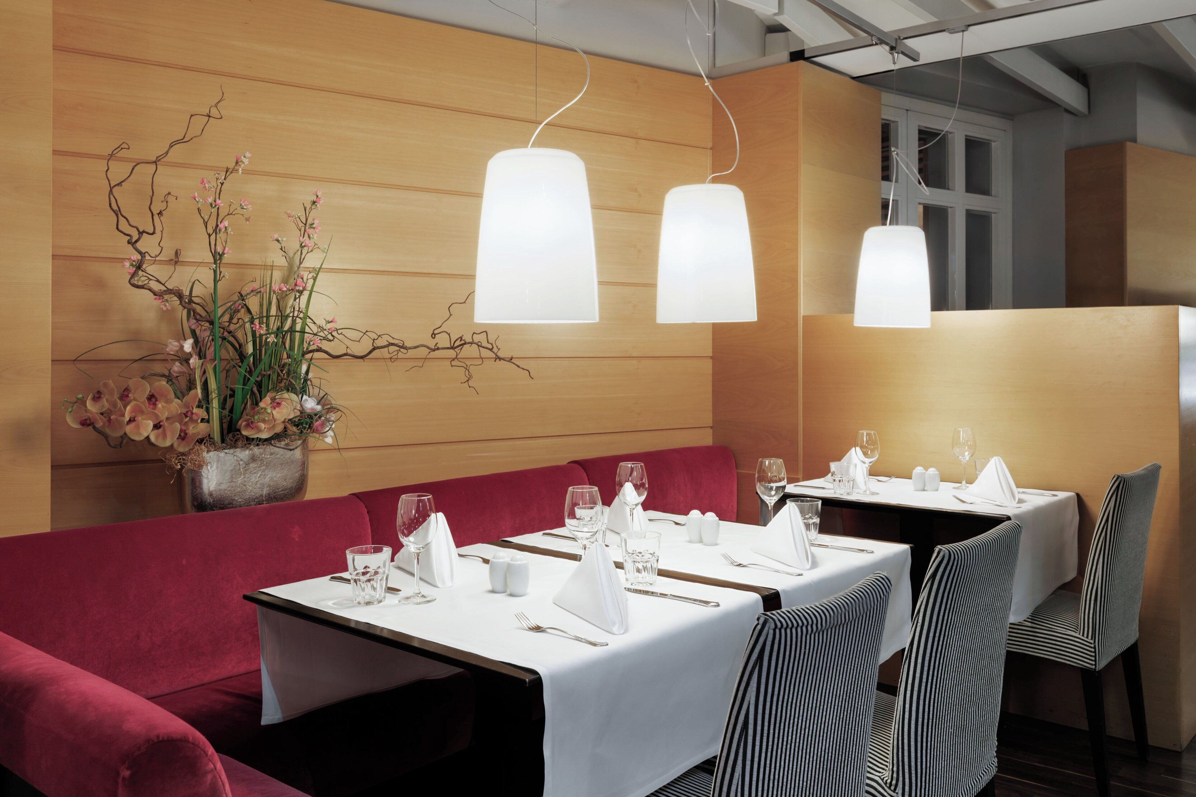 Un restaurant avec des tables dressées pour le service, un canapé rouge et des lampes suspendues.