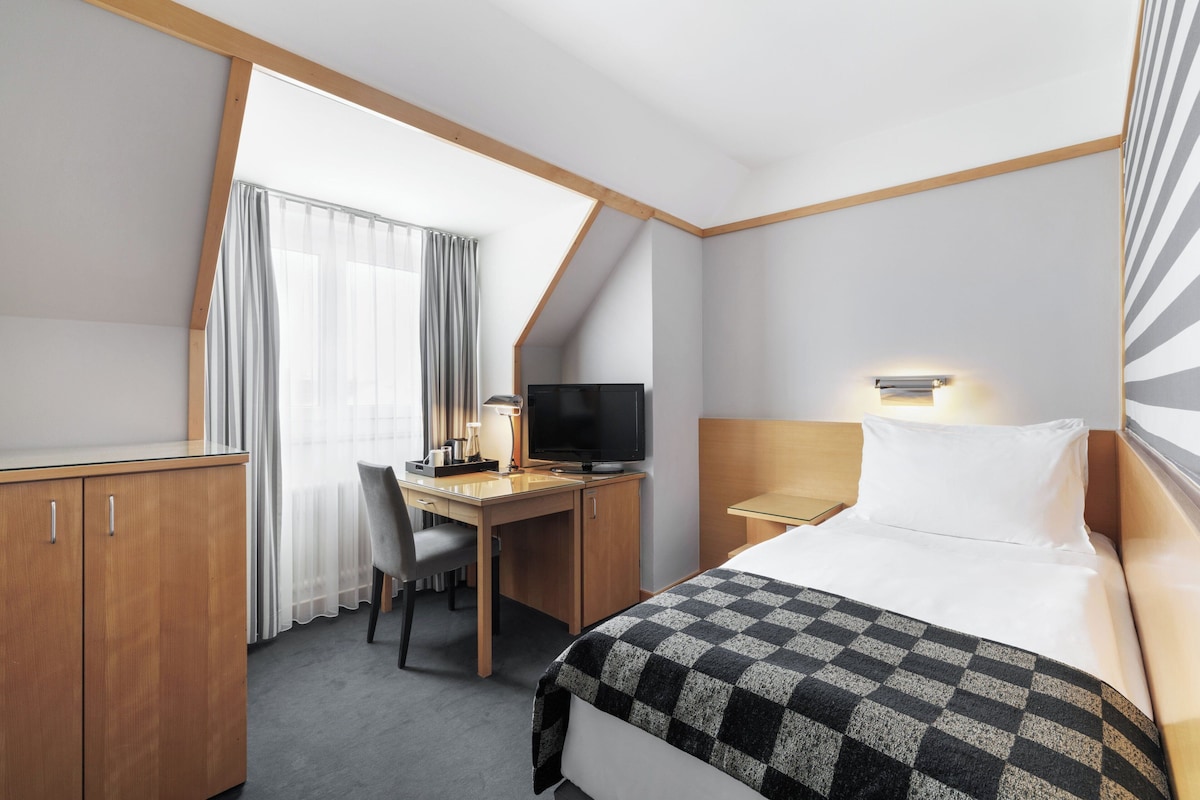 A hotel room with a bed, desk, chair, television, and a window with curtains.