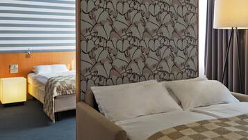 Una habitación de hotel con pared a rayas, un cabecero floral, una cama con ropa blanca, una lámpara de noche y una mesita de noche.