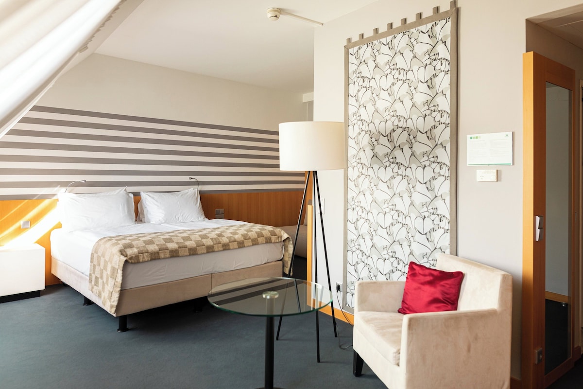 A hotel room with a bed, a small table, a sofa, a lamp, and a patterned wall.