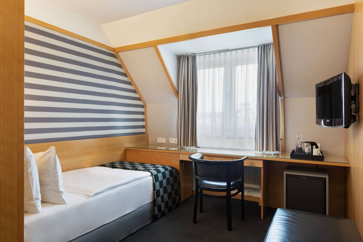 Une chambre d’hôtel équipée d’un lit, d’un bureau, d’une chaise, d’une télévision et d’un petit réfrigérateur.