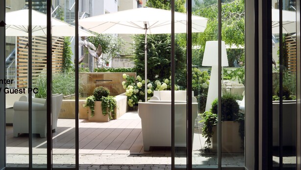 A modern outdoor patio area with white furniture, large umbrellas, and lush greenery. - Holiday Inn Vienna City by IHG (Vienna)