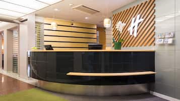 A modern reception desk with a curved design, a wooden accent, and a large 'H' logo on the wall.