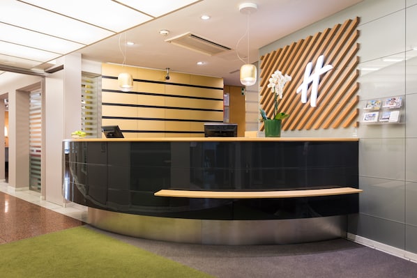 A modern reception desk with a curved design, a wooden accent, and a large 'H' logo on the wall.