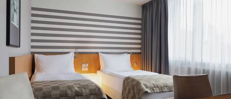 A hotel room with two beds, a wooden headboard, a large window with curtains, and a framed picture on the wall.