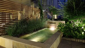 A rectangular hot tub with a wooden deck surrounding it, a wooden fence, and a small garden area with plants and a bird sculpture. - Holiday Inn Vienna City by IHG (Vienna)