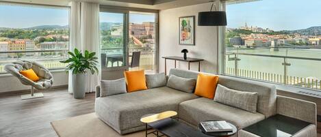 A modern living room with a grey sectional sofa, a black coffee table, and a view of a river and cityscape.