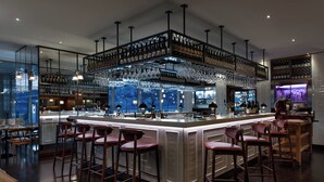 Un espace bar moderne doté d’un comptoir haut, de nombreux tabourets et d’une grande variété de bouteilles et de verres.