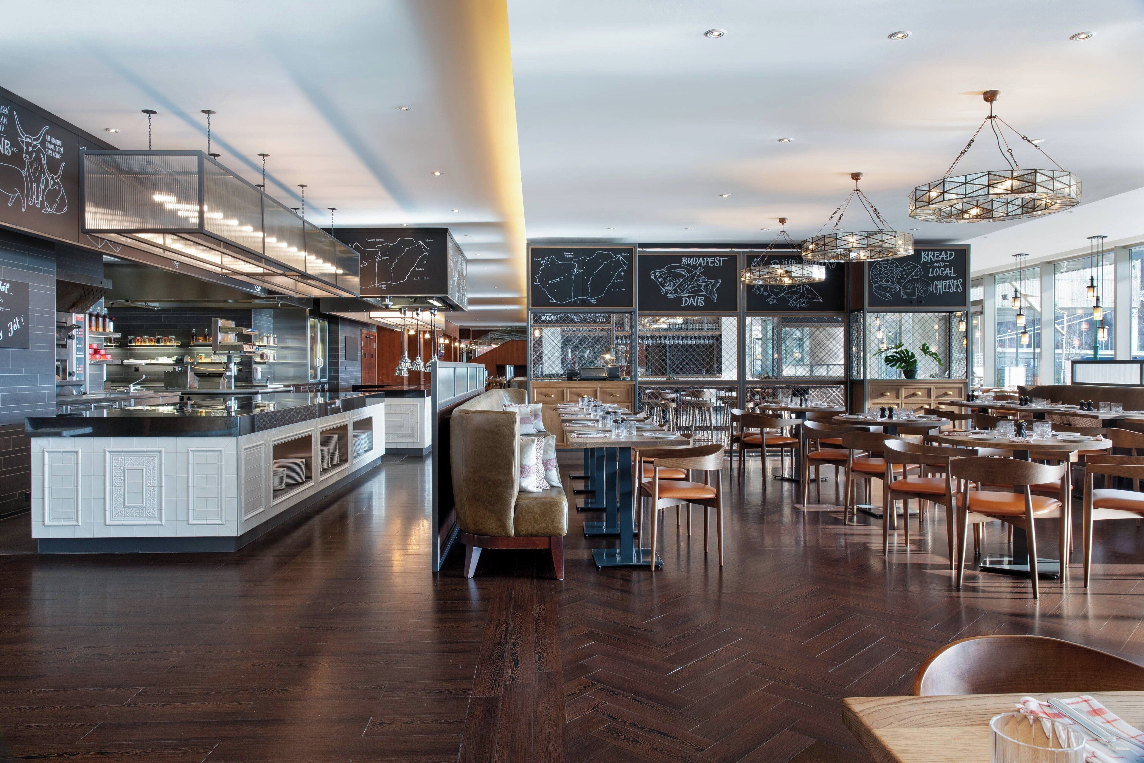 A modern restaurant with a central bar area, multiple dining tables, and a large window offering views.