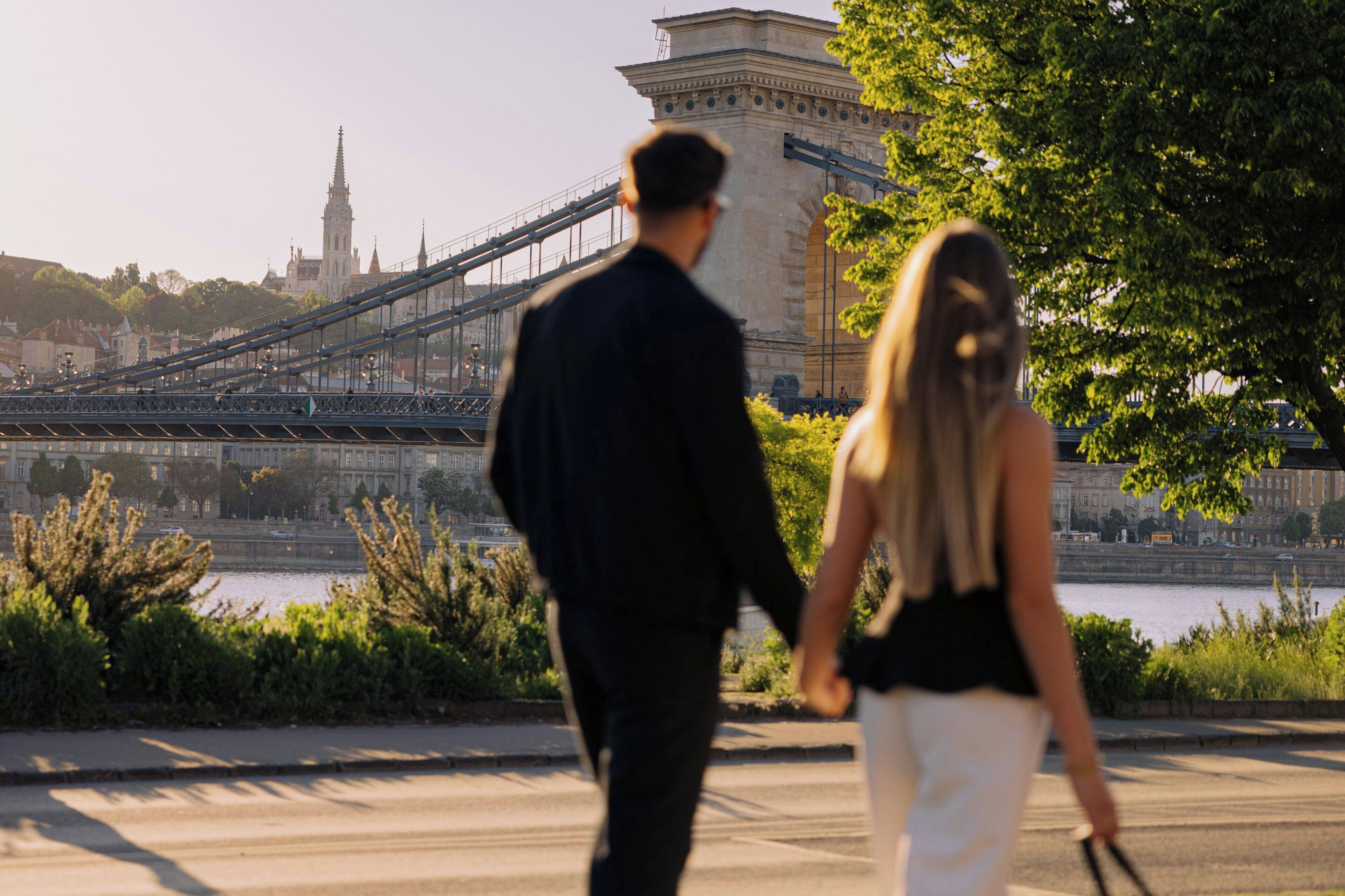 Una pareja caminando sobre un puente, con un edificio histórico al fondo.