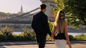 Una pareja caminando sobre un puente, con un edificio histórico al fondo.
