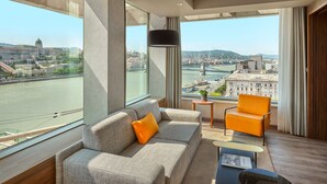 Une chambre d’hôtel moderne dotée d’une grande fenêtre donnant sur une rivière et le paysage urbain.