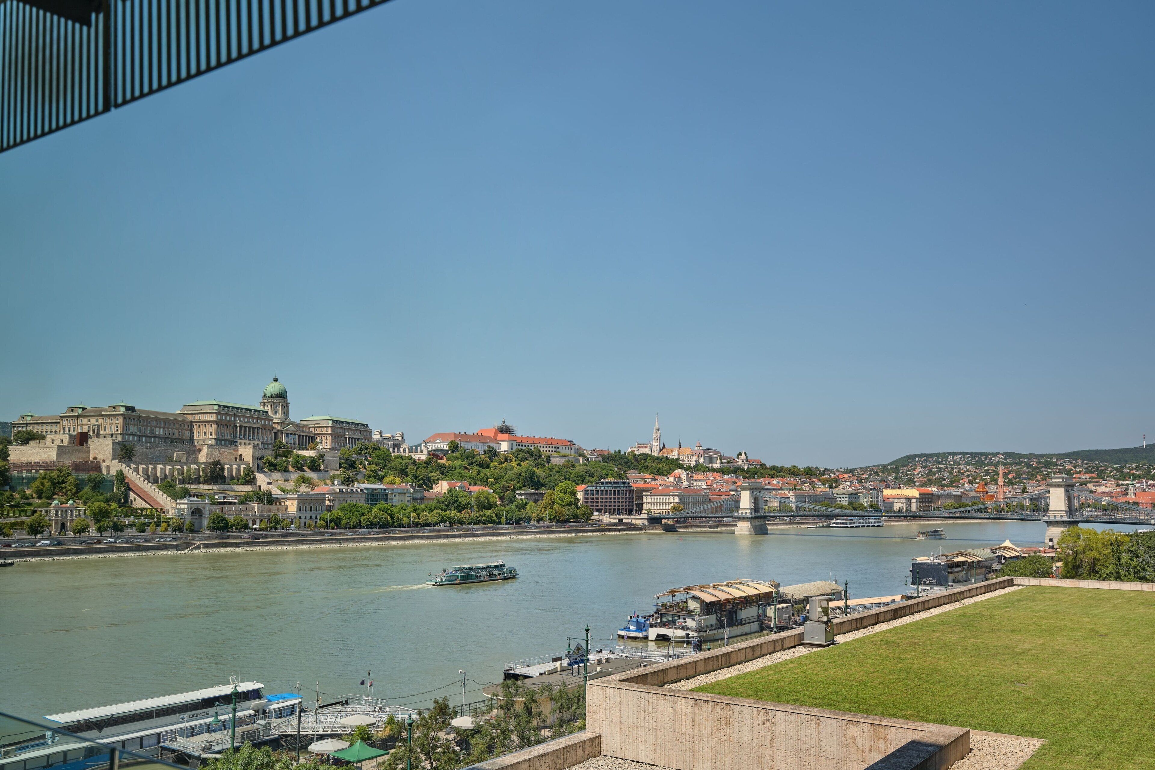 Vista del río de un complejo histórico de edificios con una gran cúpula, un puente y barcos en el agua.