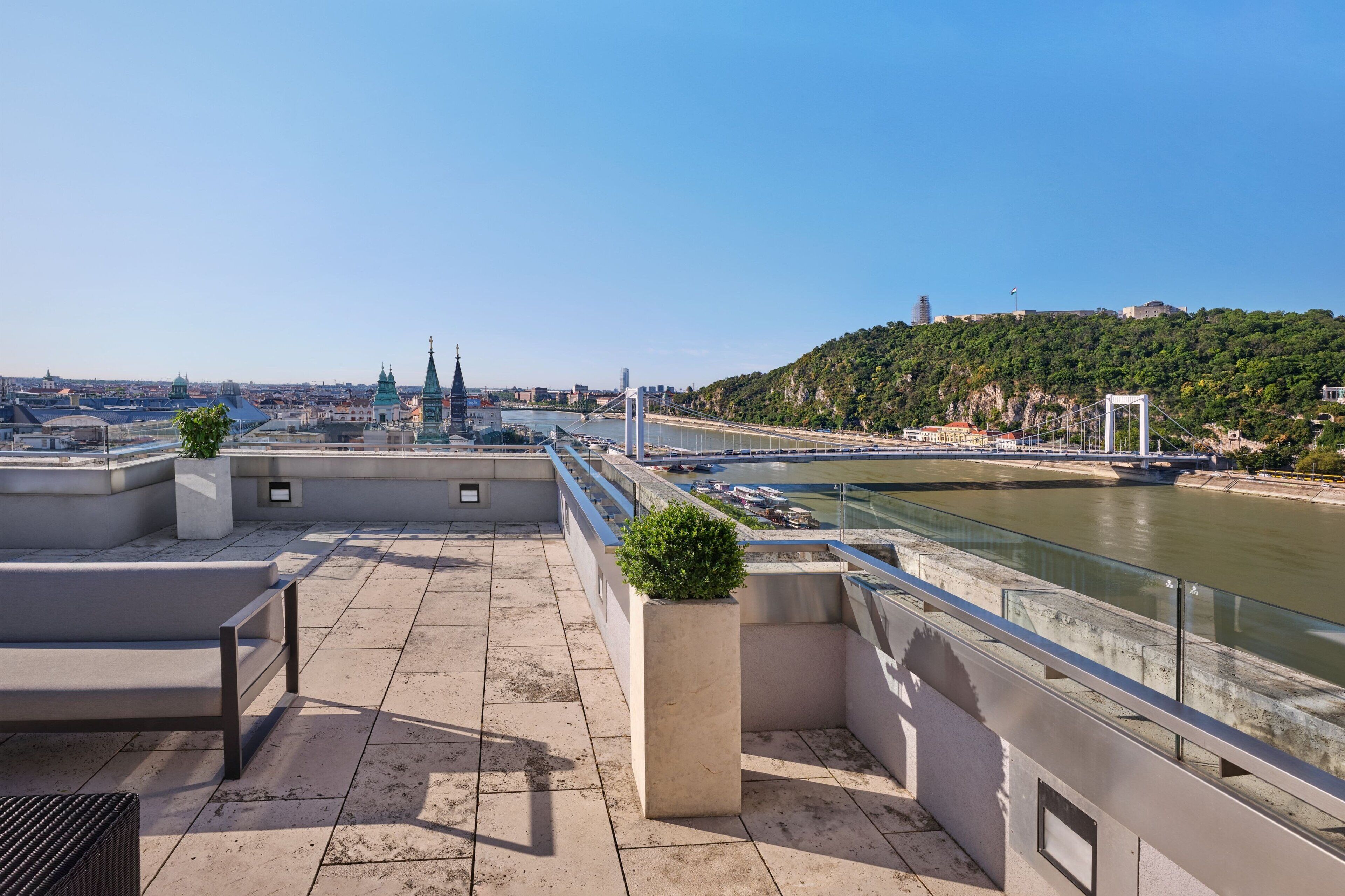 A rooftop terrace with a view of a river, a bridge, and city buildings.