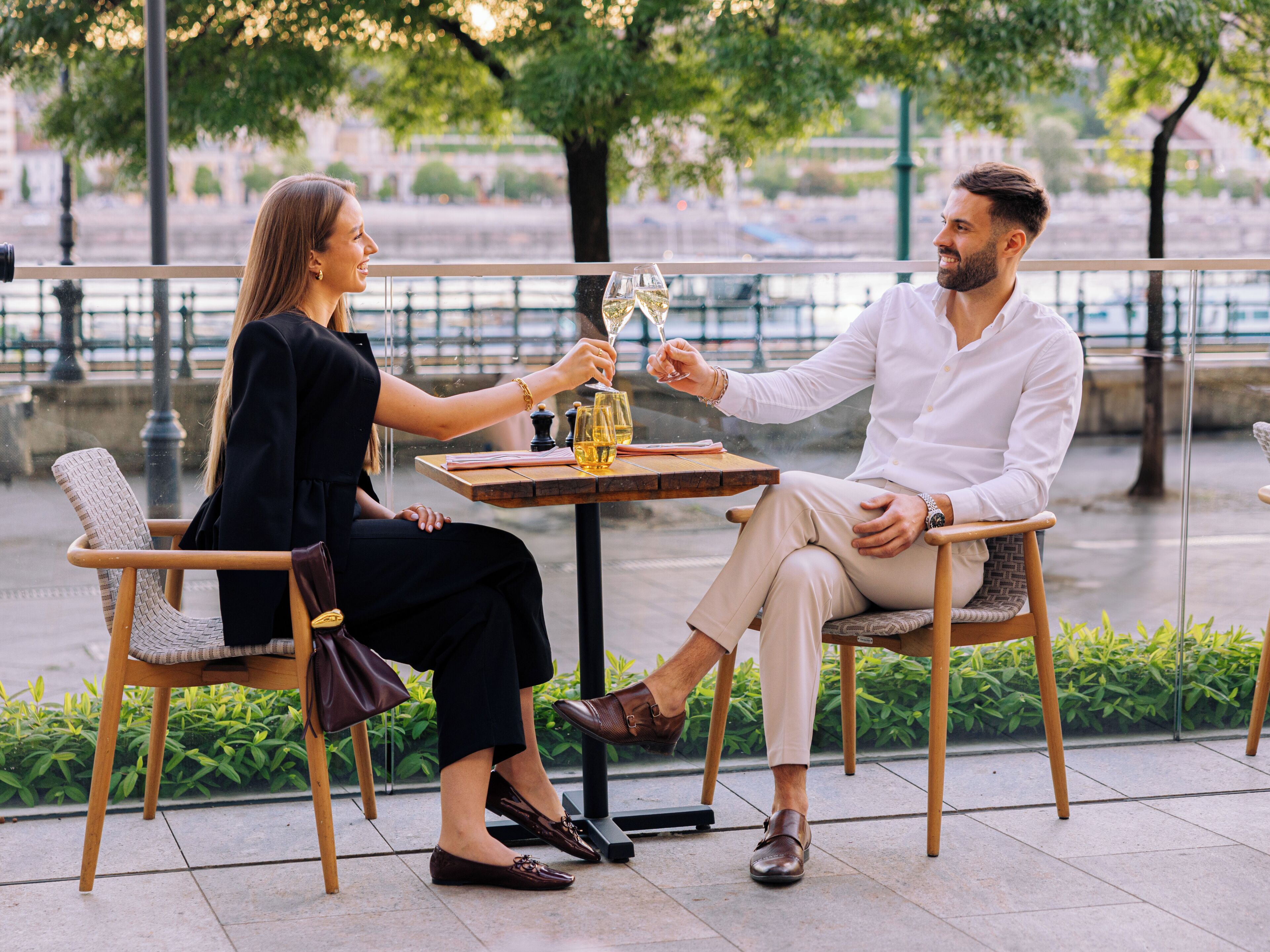 Two people seated at an outdoor table with a glass of wine, a menu, and a bottle of wine.