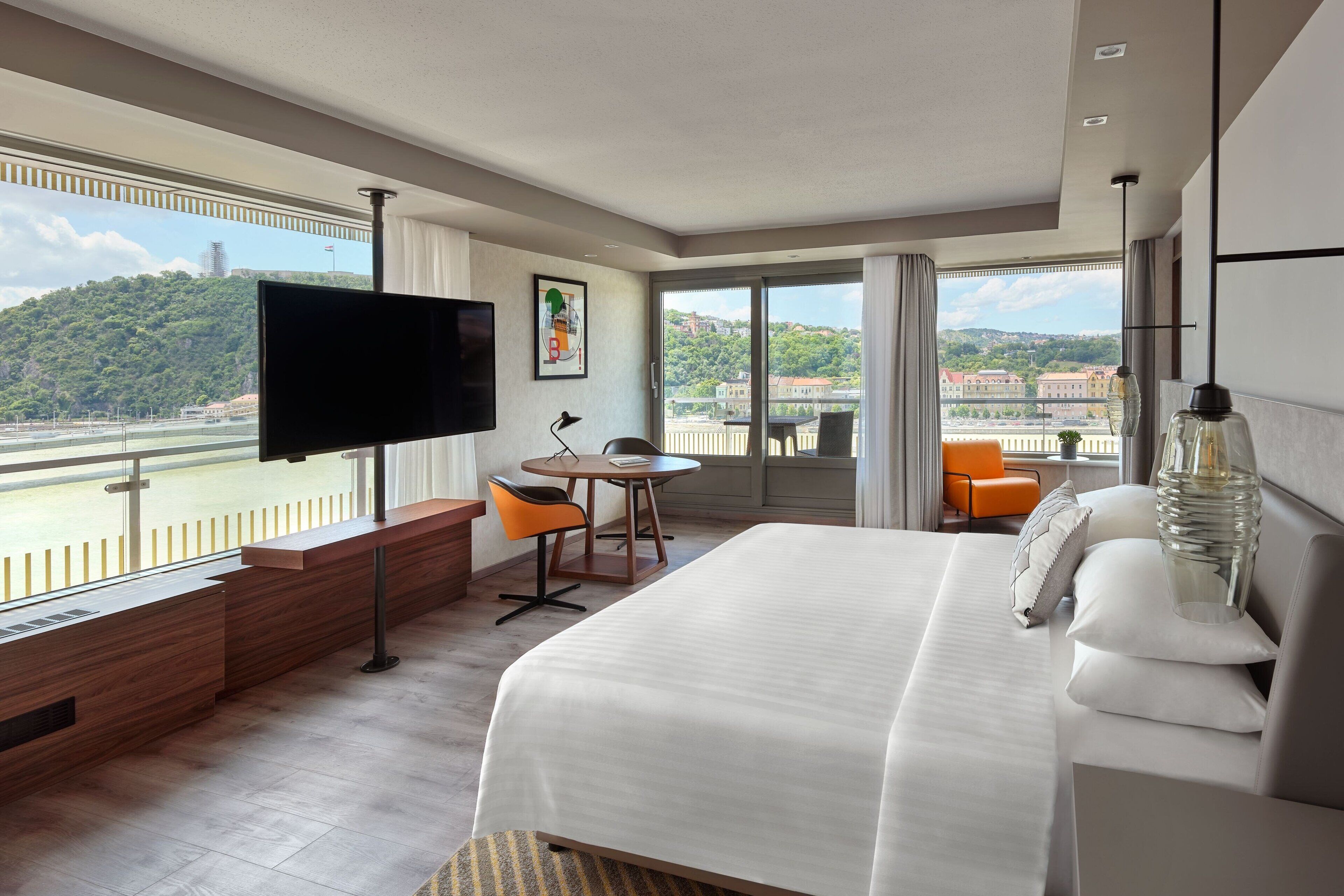 A hotel room with a large bed, a TV, a desk, and a view of a body of water.