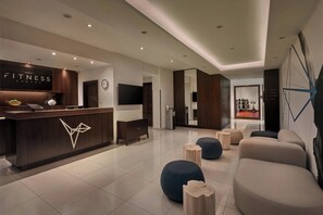 A modern fitness center with a reception desk, seating area, and exercise equipment.