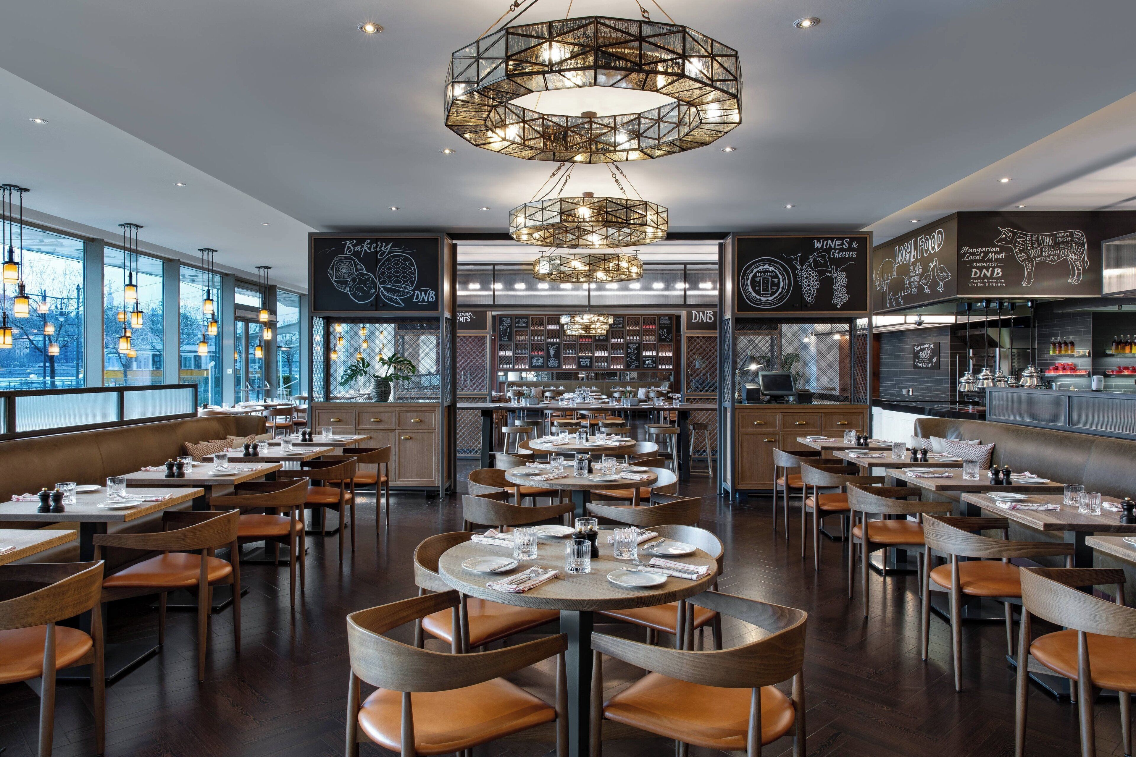 Un restaurant moderne avec des tables rondes, des chaises en bois et un lustre central.
